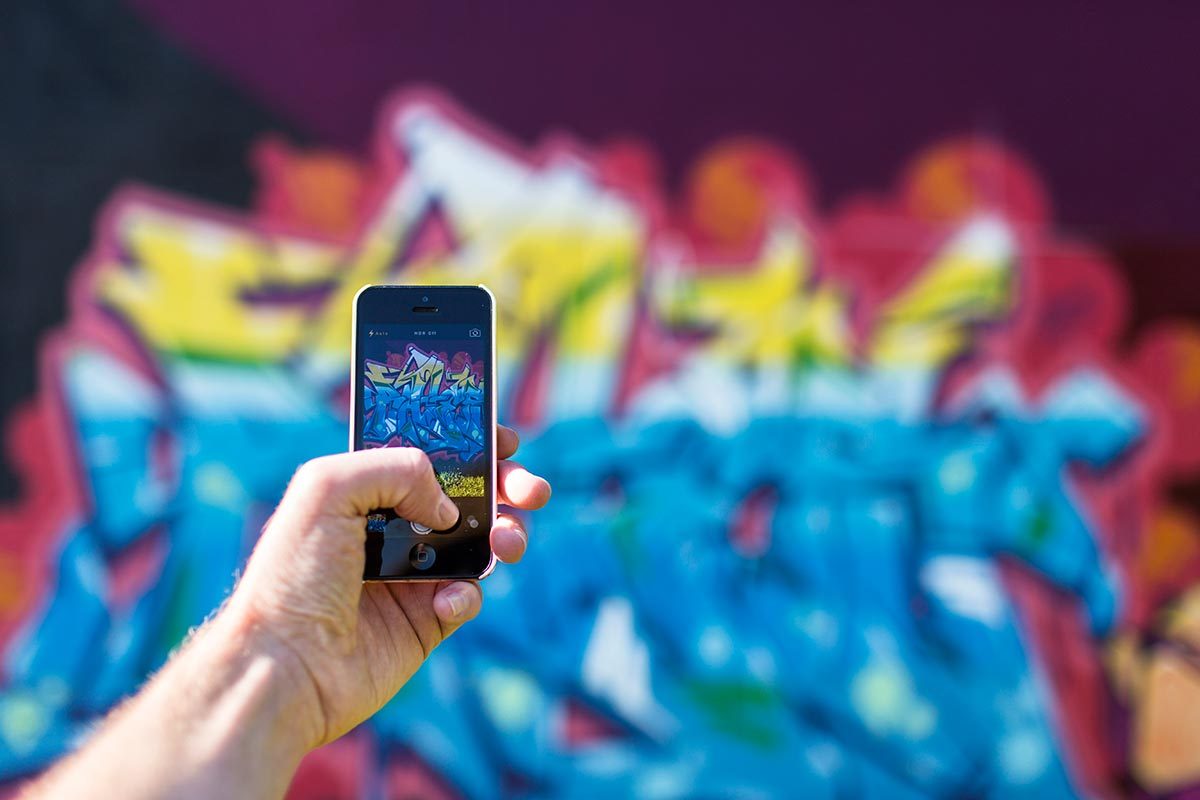 Hand holding phone taking photo of graffiti wall